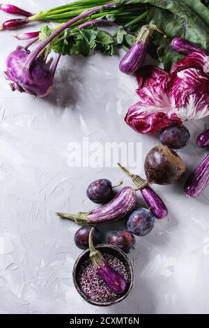 Assortimento di materie organiche viola di verdure mini melanzane, cipolline, barbabietole, insalata di radicchio, prugne, cavolo rapa, fiore di sale di cemento grigio b Foto Stock