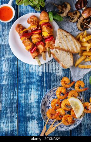 Varietà di snack barbecue il pranzo. Lastre grigliate di piccante spiedini di gamberi, pollo, maiale, verdure e funghi spiedini, pane, patate fritte patate con salse Foto Stock