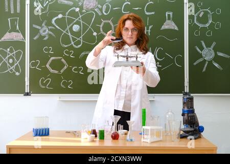 Donna scienziata chimica con bilancia in mano e matracci sul tavolo. Prove e ricerche nel laboratorio dell'università Foto Stock