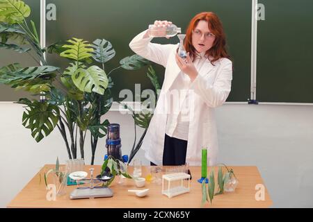 Insegnante donna sorpresa con bottiglia d'acqua in classe scolastica alla lezione di biologia. Analisi, prove e ricerche nel laboratorio scolastico Foto Stock