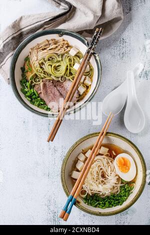 Due ciotole di zuppe in stile asiatico con noodle di soba di tè verde, uova, funghi, manzo, cipolla e formaggio tofu, servite con chopsticks e cucchiaio ove Foto Stock