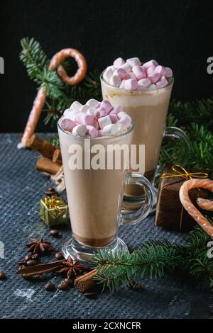 Due bicchieri di caffelatte con marshmallow rosa con decorazioni di Natale, caramelle, spezie, i chicchi di caffè e abete su texture scuro dello sfondo. Top vie Foto Stock