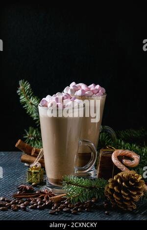 Due bicchieri di caffelatte con marshmallow rosa con decorazioni di Natale, caramelle, spezie, i chicchi di caffè e abete su texture scuro dello sfondo. Top vie Foto Stock