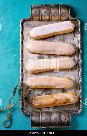 In casa Caffè eclairs con smalto diversi su vintage vassoio di metallo su legno color turchese sfondo con copia spazio. Vista dall'alto. Foto Stock