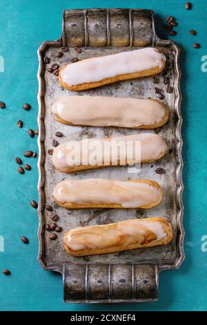 Caffè fatto in casa eclairs con diversi smalto, con chicchi di caffè su vassoio di metallo vintage su sfondo di legno turchese con spazio copia. Vista dall'alto. Foto Stock