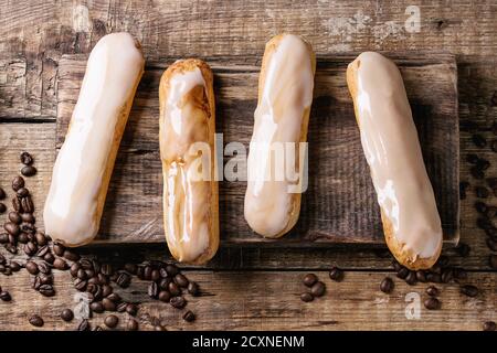 Freschi Fatti in casa eclairs caffè con diversi smalti e i chicchi di caffè su legno tagliere sopra il vecchio legno sfondo texture con spazio per il testo. A Foto Stock