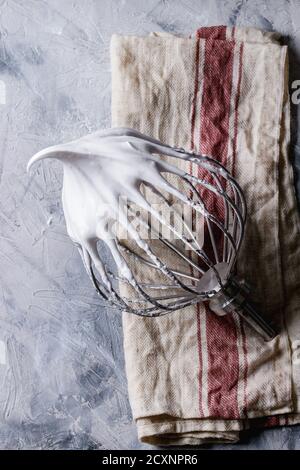 Processo di cottura meringa. Montare gli albumi sul mixer sbattere su un asciugamano di lino su uno sfondo grigio. Vista dall'alto. Concetto di dessert da forno Foto Stock