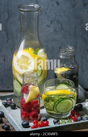Agrumi cetrioli bacche mirtillo e lampone sassy acqua sassi per detox in bottiglie di vetro su sfondo blu di legno. Mangiare pulito, stile di vita sano Foto Stock