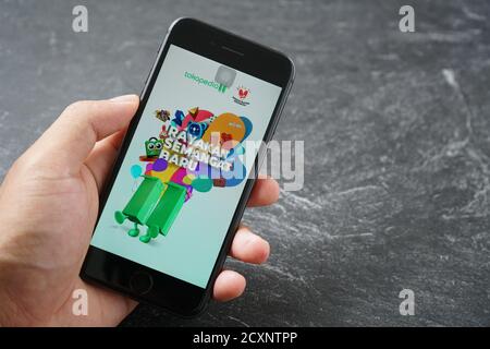 Mataram, Indonesia - 1 ottobre 2020: Mano che tiene Apple iPhone 8 con il marketplace tokopedia negozio on-line sullo schermo su pietra pad, vista dall'alto. Foto Stock