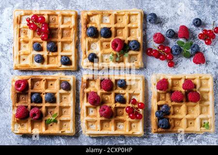 In casa piazza cialde belghe con fresche bacche mature mirtillo, lampone, ribes rosso su grigio Sfondo texture. Vista da sopra con uno spazio Foto Stock