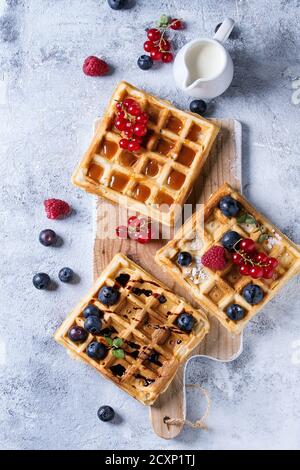 Waffle belgi quadrati fatti in casa con frutti di bosco freschi maturi, mirtillo, lampone, ribes rosso servito con caramello, salsa balsamica su tavola di legno Foto Stock