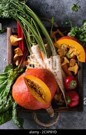 Variety of autumn harvest vegetables carrot, parsnip, chard, paprika, hokkaido pumpkin, porcini and chanterelles mushrooms in wooden tray over gray te Stock Photo