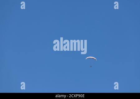 Parapendio con un'ala bianca che scivola nell'aria di fronte a un cielo blu durante un pomeriggio soleggiato. È uno degli sport aerei estremi. Immagine del parag Foto Stock