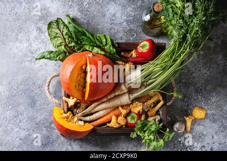 Variety of autumn harvest vegetables carrot, parsnip, chard, paprika, hokkaido pumpkin, porcini and chanterelles mushrooms in wooden tray over gray te Stock Photo