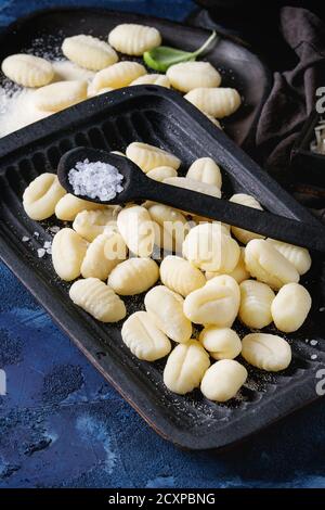 Gnocchi di patate crudi non cotti in piatti di legno nero con ingredienti. Farina, basilico, sale su fondo di cemento blu scuro. Cucina casalinga. Foto Stock