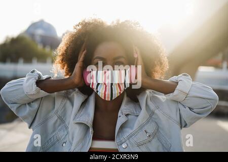 Ragazza nera che ascolta la musica con le cuffie mentre indossa la maschera facciale Outdoor - concetto di stile di vita Coronavirus Foto Stock