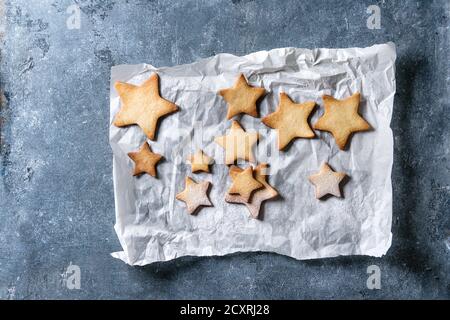 Biscotti fatti in casa shortbread a forma di stella zucchero di dimensioni diverse con polvere di zucchero su carta da forno su consistenza blu sfondo. Natale trattamento sfondo Foto Stock