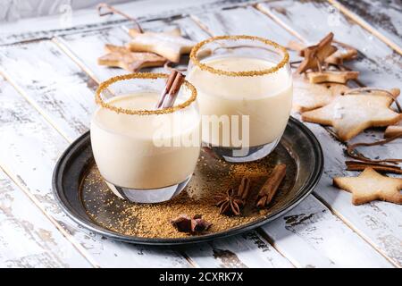 Cocktail al latte di Natale con cannella, servito in due bicchieri su vassoio vintage con biscotti allo zucchero a forma di stella di shortbread di dimensioni diverse su bianco Foto Stock