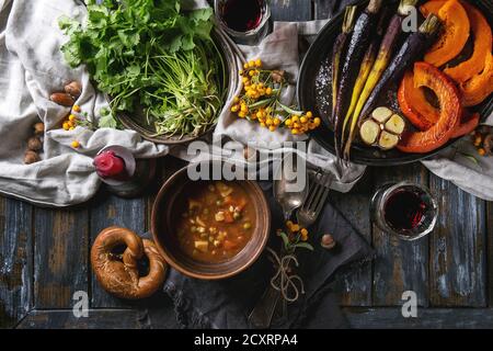 Holiday tabella di impostazione di decorazione con ciotole di zuppa calda, cottura zucca, carota, aglio, coriandolo fresco, salatini pane, vino rosso, bacche e candela Foto Stock