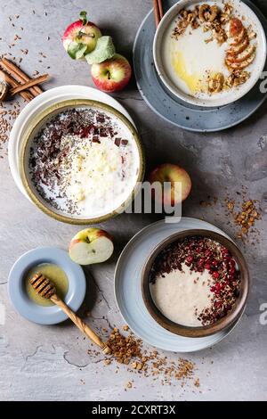 Varietà ciotole di latte cereali porridge con diversi additivi, servito con mele, bacche e i semi di più grigio tavolo da cucina. Vista da sopra con uno spazio Foto Stock