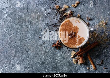 Bicchiere di vetro di tradizionale indiano Masala chai tè con gli ingredienti di cui sopra. La cannella, cardamomo, anice, zucchero, tè nero più scuro dello sfondo texture. Parte superiore Foto Stock