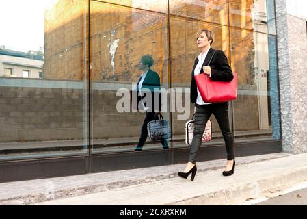 Donna che cammina con la borsa di un computer portatile accanto all'edificio dell'ufficio Foto Stock