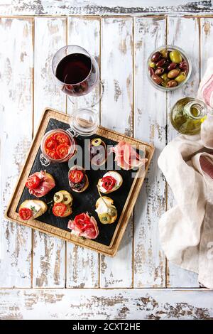 Le tapas o bruschetta varietà. Fette di pane con prosciutto, pomodori secchi, olio di oliva, olive, pepe su legno di ardesia che serve la scheda con un bicchiere di rosso wi Foto Stock