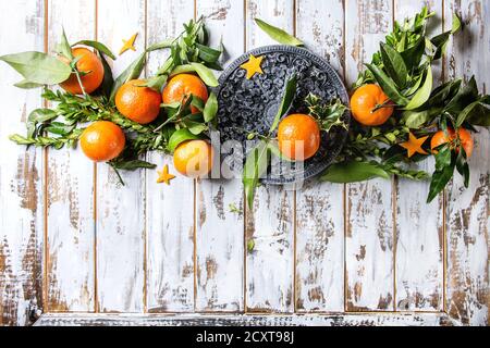 Decorazioni natalizie con clementine o tangerini con foglie e rami verdi su tavola nera ornata su tavola in legno bianco. Via superiore Foto Stock
