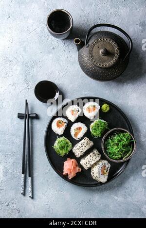 In casa sushi set di rulli con salmone, i semi di sesamo che serve nella piastra nera con rosa di zenzero sott'aceto, la salsa di soia, wasabi, insalata di alghe marine, bastoncini su gr Foto Stock