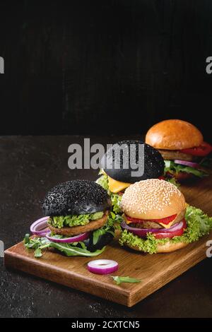 Set di hamburger fatti in casa in bianco e nero e panini con avocado, salsa di pomodoro, lattuga, rucola, formaggio, cipolla su legno che serve scheda sopra la tabella scuro. Rus Foto Stock