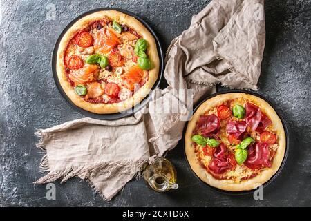 Due tradizionale pizza con bresaola, salmone affumicato, formaggio, pomodori e basilico servito su piastre nere con tessuto nero su sfondo di texture. Parte superiore Foto Stock