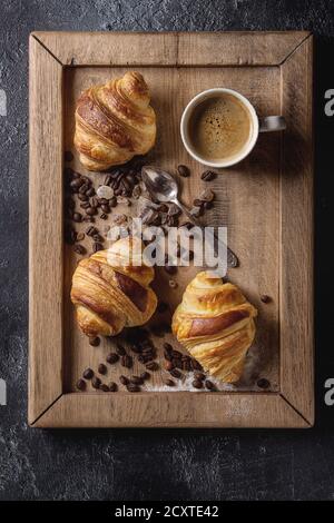 Freschi di forno cornetti tradizionali e la tazza di caffè espresso, caffè, zucchero sul vassoio in legno nero su sfondo di texture. Vista superiore, spazio Foto Stock
