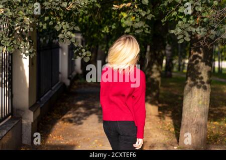 giovane donna bionda in caldo maglione all'aperto. vista dal retro. i capelli della donna sono illuminati dal sole d'autunno. Foto Stock