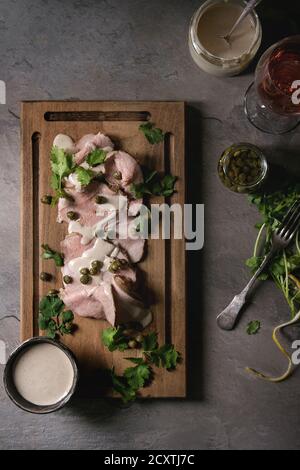 Vitello tonnato piatto italiano. Sottili fette di vitello con salsa di tonno, capperi e coriandolo servita su legno scheda servente, bicchiere di vino rosato e ingrediente Foto Stock
