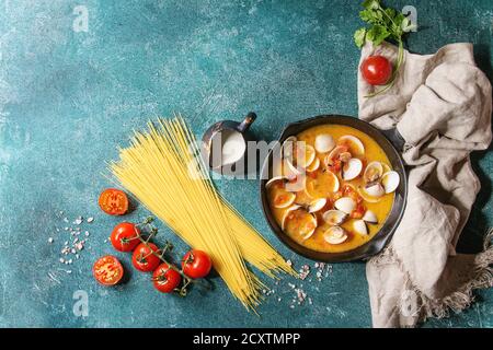 Vongole in crema di pomodoro sugo per la pasta in ghisa pan con tessili e gli ingredienti per cucinare gli spaghetti sopra turchese sfondo texture. T Foto Stock