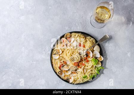 Pasta Spaghetti vongole in crema di pomodoro salsa in lamiera nera con una forchetta e un bicchiere di vino bianco grigio Sfondo texture. Vista superiore, spazio di copia Foto Stock