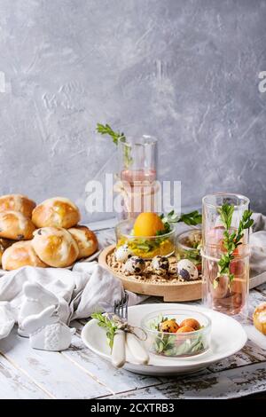 Pasqua messa in tavola con colorate di arancione uova, dolci tradizionali, rami verdi decorate, Vuoto piastra bianca con posate, bicchiere di limonata bere oltre Foto Stock