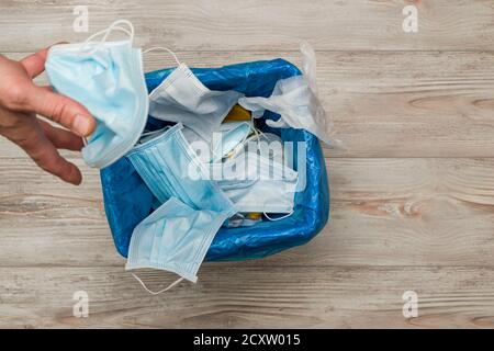 Mano dell'uomo gettando la maschera chirurgica usata nella spazzatura. Foto Stock