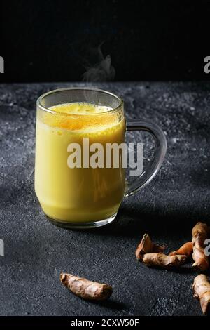 Tazza di bevanda ayurvedica golden latte curcuma latte con curcuma in polvere e gli ingredienti di cui sopra nero su sfondo di texture. Foto Stock