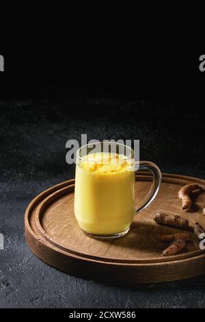 Tazza di bevanda ayurvedica golden latte curcuma latte con curcuma in polvere il round vassoio in legno e gli ingredienti di cui sopra nero su sfondo di texture. Copia s Foto Stock