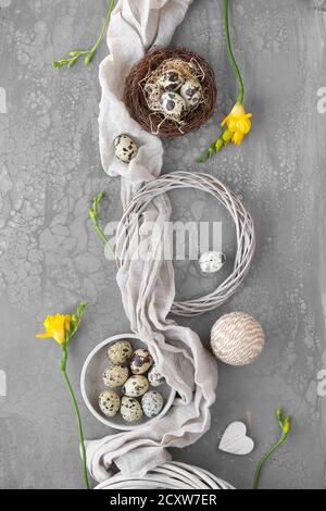 Appartamento di Pasqua con uova di quaglia in nido d'uccello con tessuto di lino. Fiori di freesia gialla e corona di rattan. Foto Stock