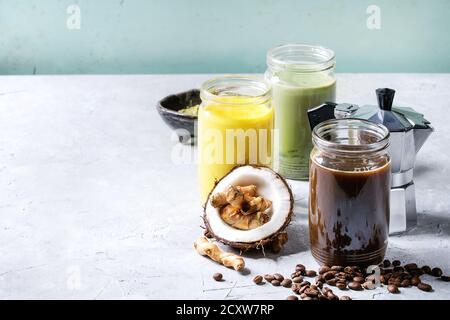 Varietà di iced colorato latte bevande. Caffè ghiacciato, curcuma e matcha latte cocktail in vasi di vetro con gli ingredienti sopra in grigio verde texture b Foto Stock