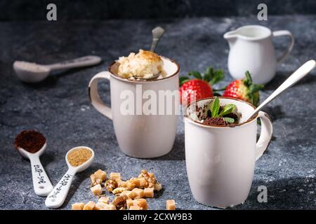 Cioccolato e vaniglia e caramello mug dolci da forno a microonde con fragole fresche e gli ingredienti sopra in blu tavolo da cucina. Close up Foto Stock