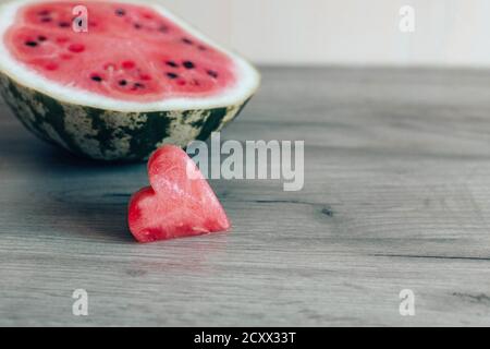 Fresco fetta matura di anguria a forma di cuore su legno sfondo e metà di cocomero sullo sfondo Foto Stock