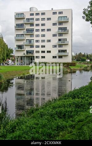 Spijkenisse, Paesi Bassi, 30 settembre 2020: Edificio di appartamenti a nove piani con intonaco bianco che si riflette nelle acque di un canale vicino Foto Stock