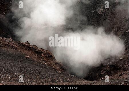 I turisti che esplorano le zone al di sotto della pericolosa cima dell'Etna, la Sicilia, l'Italia, sono avvertiti di evitare i bordi di crateri, fessure e sfiati che fiaccano le nuvole di vapore e gas dal profondo all'interno della montagna. I visitatori possono accedere alle zone autorizzate del cratere "‘safe" a 9,590 m in funivia o minibus 4x4 e partecipare a visite guidate ufficiali a piedi, anziché rischiare di spostare da soli cenere, legnoli e pietre sciolte. L'Etna, il vulcano attivo più alto d'Europa, è in eruzione da circa 500,000 anni, con molte recenti eruzioni da sfiati sui fianchi e dalla cima. Foto Stock