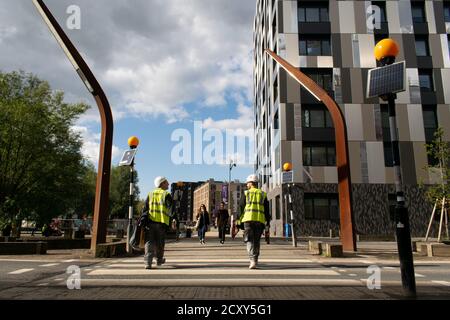 I lavoratori edili attraversano la zebra attraversando Old Mill Street che conduce al porto turistico di New Islington, Manchester UK. . Weavers Quay appartamenti Foto Stock