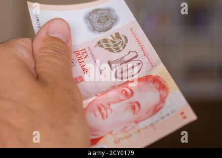 Le persone mano dando la valuta del Singapore - una nota rossa di dieci dollari sparso su uno sfondo marrone. Cambio di denaro. Foto Stock