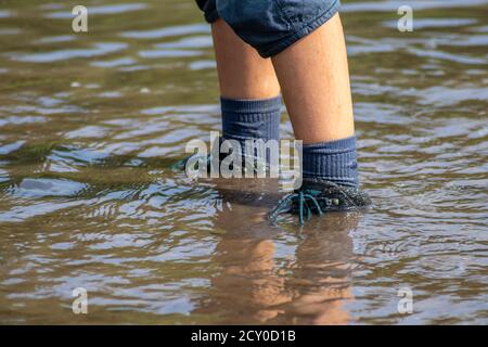 Ragazzo giovane che guidi attraverso l'alta marea con gumboot blu dopo un'alluvione ha rotto la diga di protezione e traboccante il paesi bassi o costa dell'oceano Foto Stock