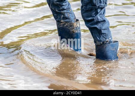 Ragazzo giovane che guidi attraverso l'alta marea con gumboot blu dopo un'alluvione ha rotto la diga di protezione e traboccante il paesi bassi o costa dell'oceano Foto Stock